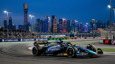 Formula 1 race car with cryptocurrency logos on track with Middle Eastern skyline